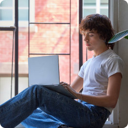 Ung person sitter i et åpent vindu og holder en PC