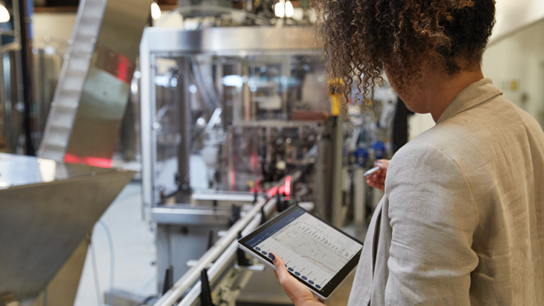 Se observa una mujer que sostiene un dispositivo Surface Pro en un entorno industrial