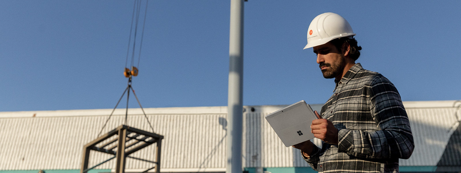 Se muestra un trabajador con casco que trabaja con un dispositivo Surface Go 2 en una zona industrial