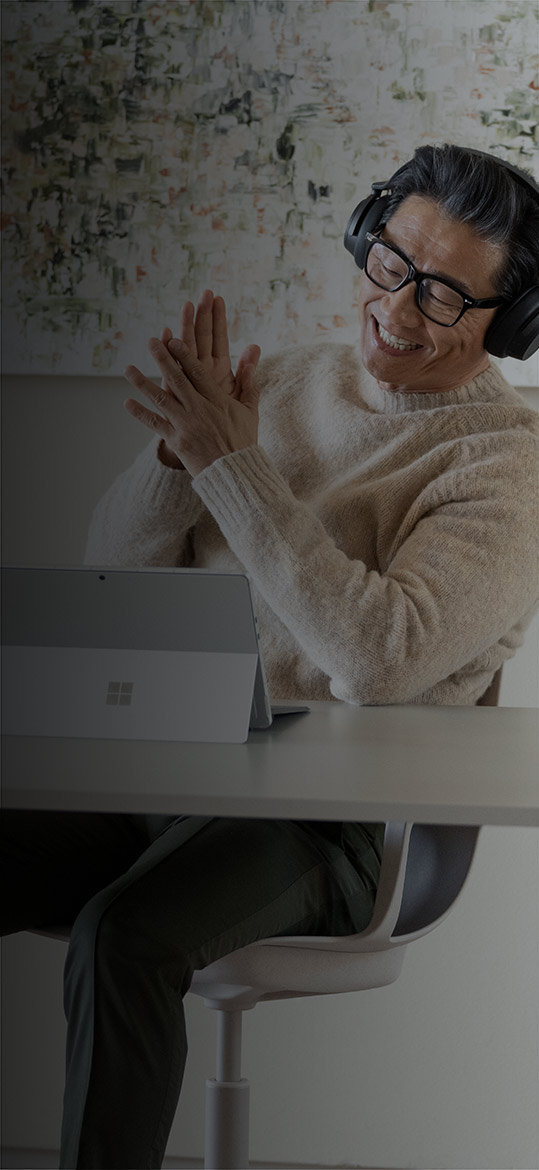 Mies istuu kotitoimistossaan nauttien Surface Pro 9 -laitteestaan käyttäen Surface Headphones 2+ -kuulokkeita