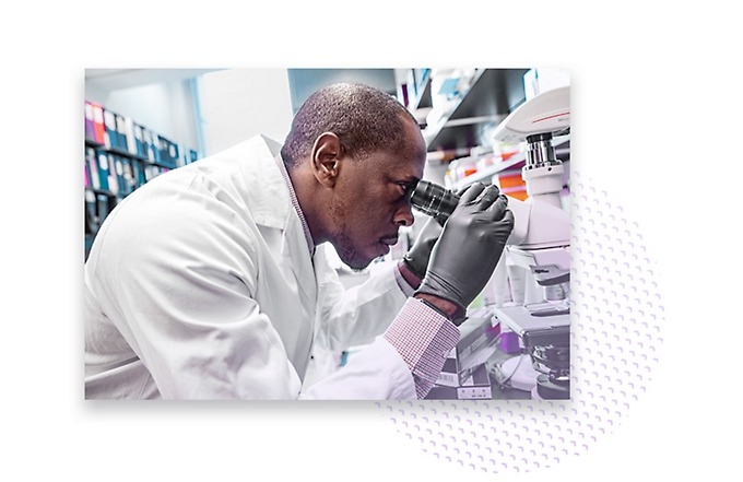 A scientist wearing a white coat looking into a microscope