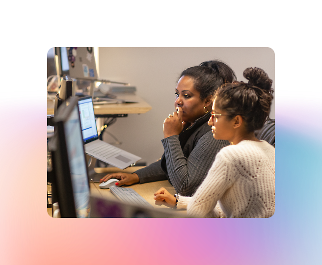 Dos mujeres concentradas en una pantalla de un ordenador en una oficina. Una teclea mientras la otra observa atentamente