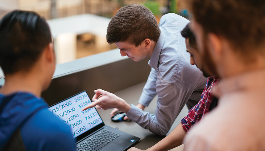 A person who has low vision points to a laptop screen while talking to coworkers. 