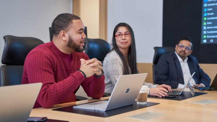 Group of people at a conference table with laptops who appear to be having a healthy and positive discussion or meeting