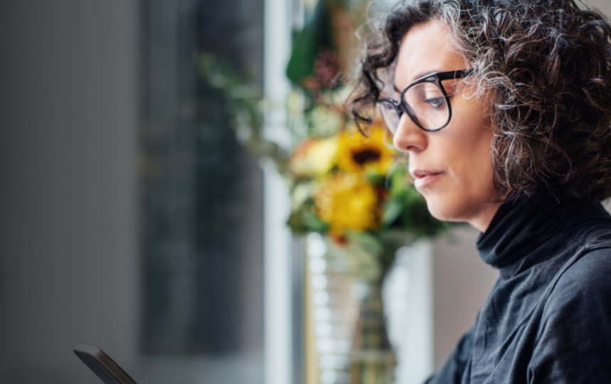 Una mujer de negocios mira el teléfono móvil mientras trabaja sentada con un equipo portátil.