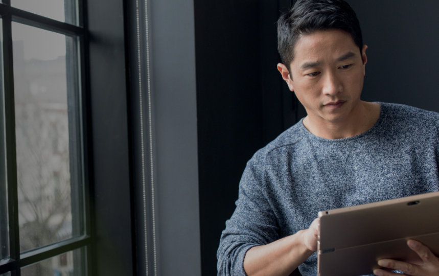 Gros plan d’un homme qui travaille sur une tablette, près d’une fenêtre.