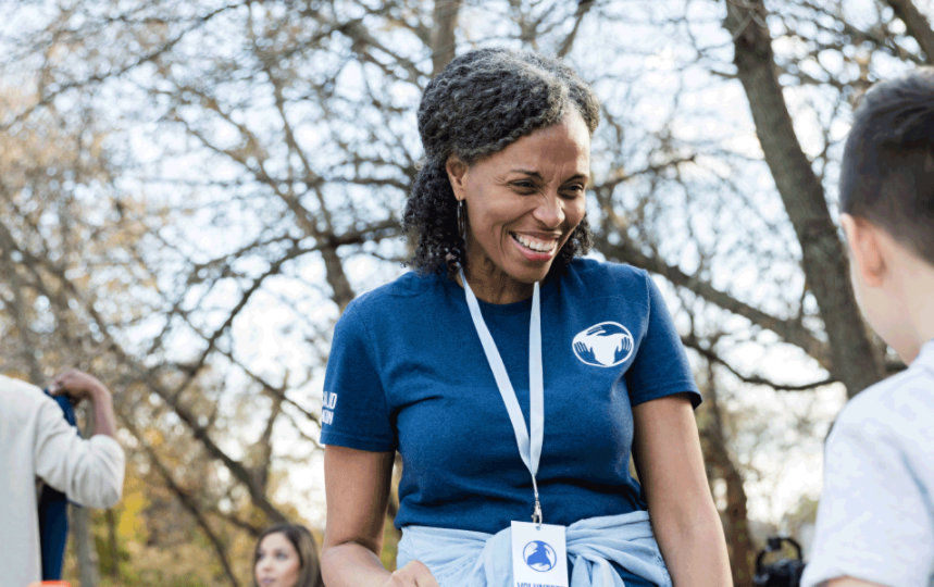 Una voluntaria sonriente delante de un niño, entre otras personas, al aire libre.