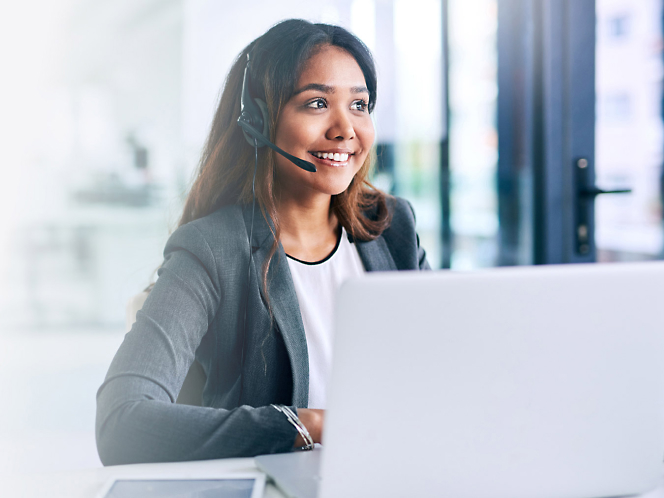 A woman wearing a headset while working on a laptop.