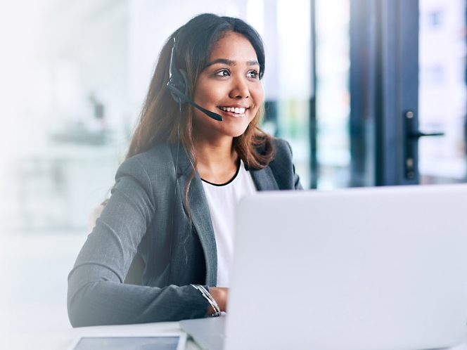 Uma mulher usando um headset enquanto trabalha em um laptop.