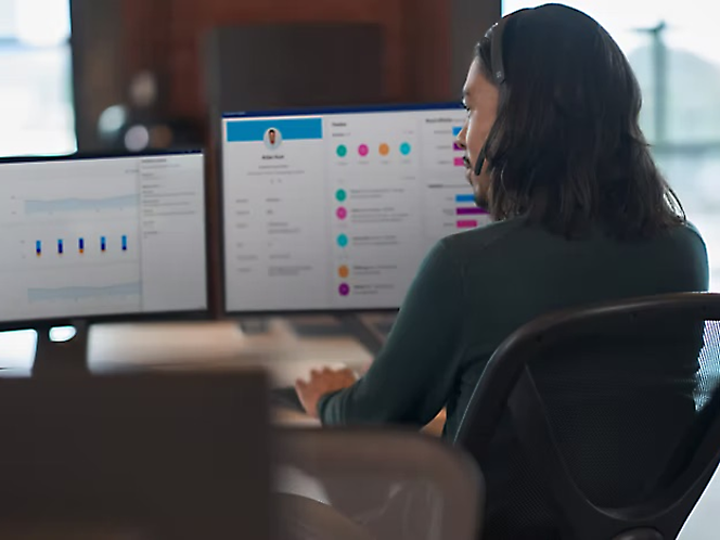 A person working at a desk with dual monitors displaying graphs and project management tools.