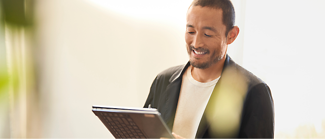 En mand smiler, mens han kigger på en tablet i et oplyst rum