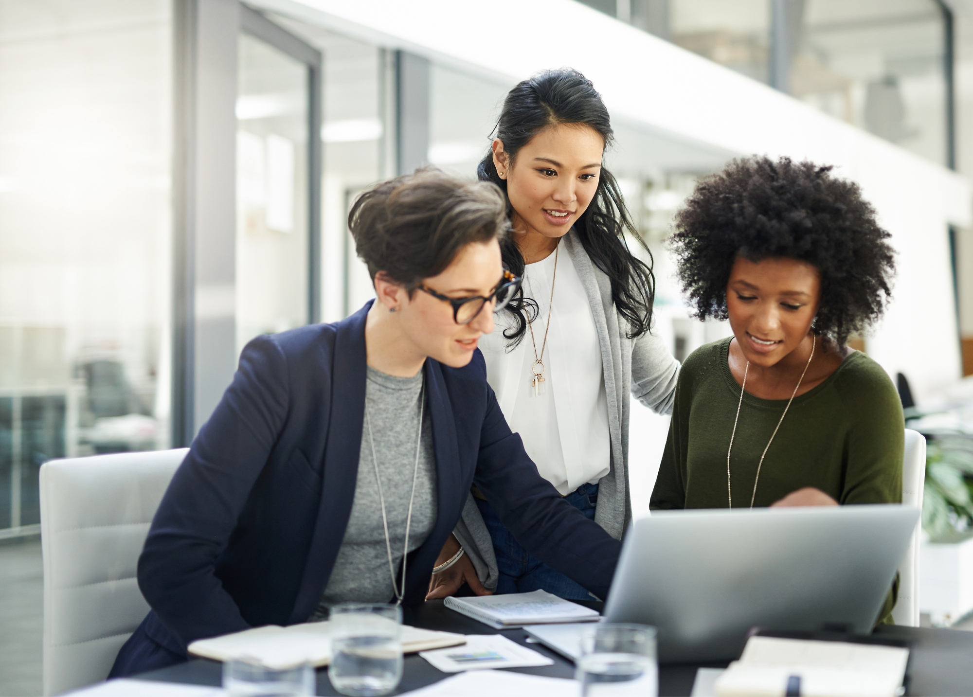 Three business professionals collaborating at a laptop in a modern office setting.