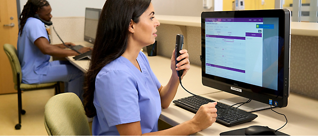 Two people in scrubs using computer and phone.