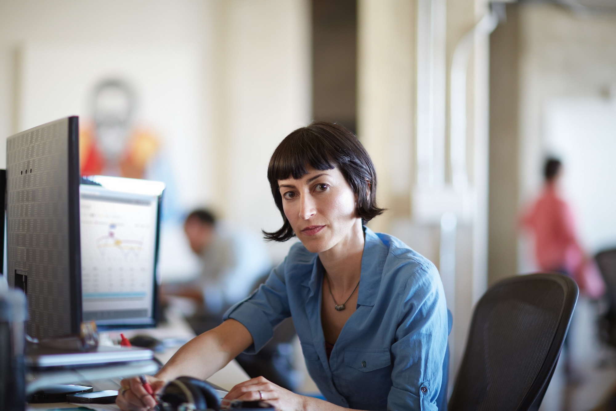 Kvinde, der koncentrerer sig om en tablet ved sit skrivebord med et lyst vindue i baggrunden.