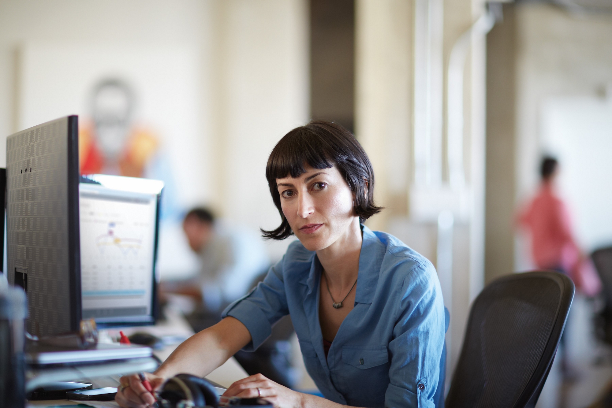 Woman concentrating on a tablet at her desk with a bright window in the background.