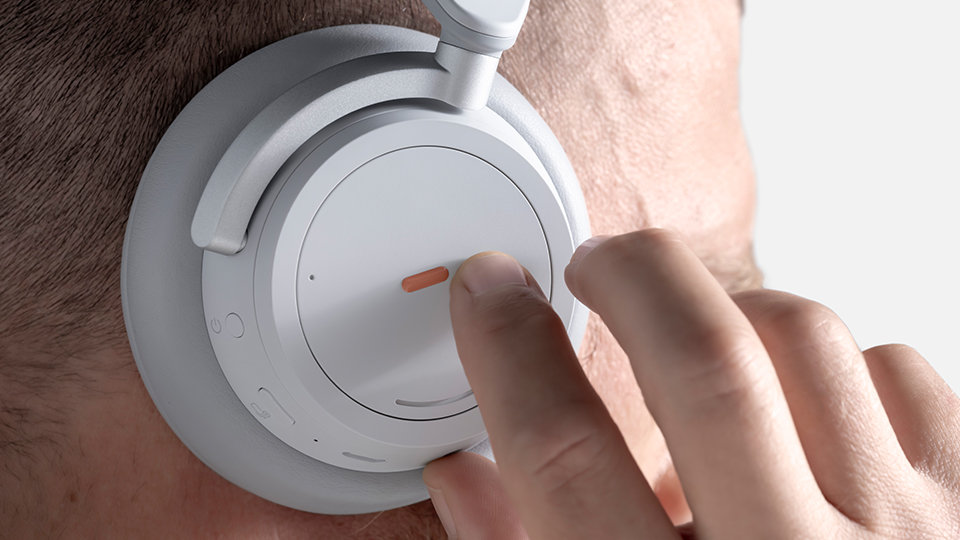 Ręka osoby dotykającej etykiety z zestawu przystosowującego do Surface na nauszniku słuchawek Surface Headphones.