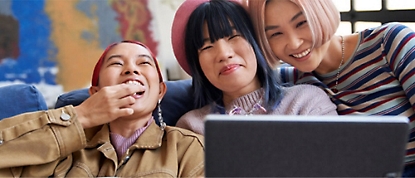 Three asian women sitting on a couch with a laptop.