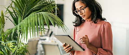 A woman in glasses is using a tablet in front of a plant.