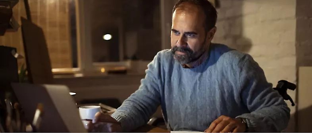 Una persona con una taza en la mano trabajando con un portátil