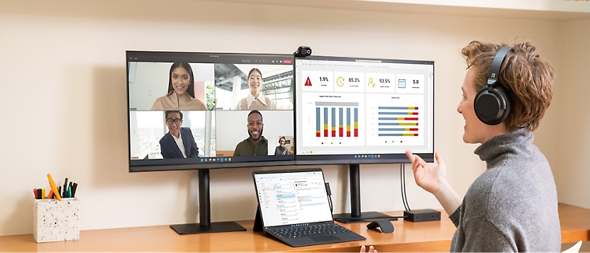 A person wearing headphones participates in a video conference call with four others displayed on a dual monitor setup.