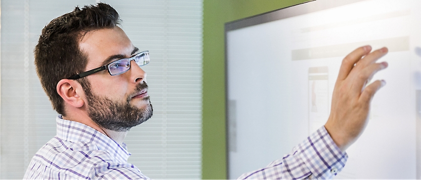 A man in glasses and a plaid shirt uses a touchscreen device.