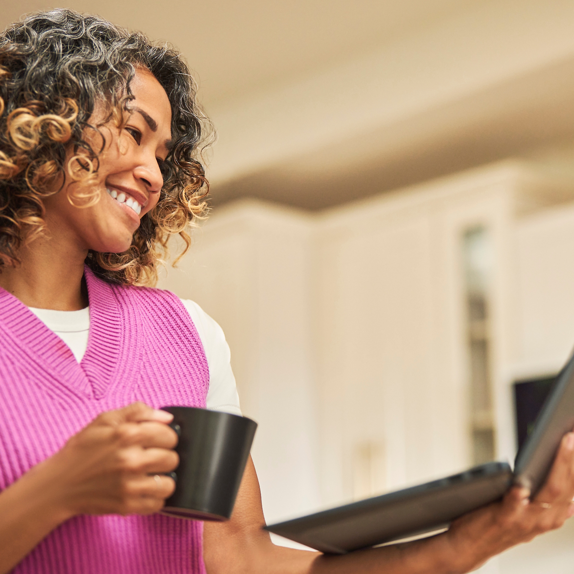 Una donna sorridente con una tazza di caffè in mano e un portatile nell'altra