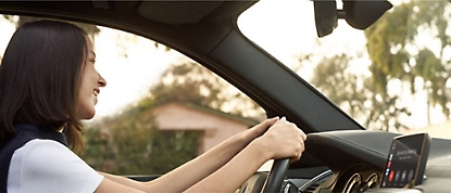 Een vrouw die in een auto rijdt met haar handen op het stuur.