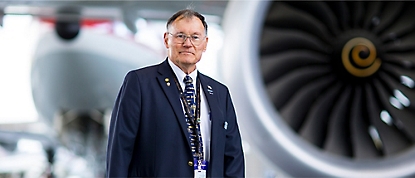 Um homem usando terno em pé na frente de um motor de avião.