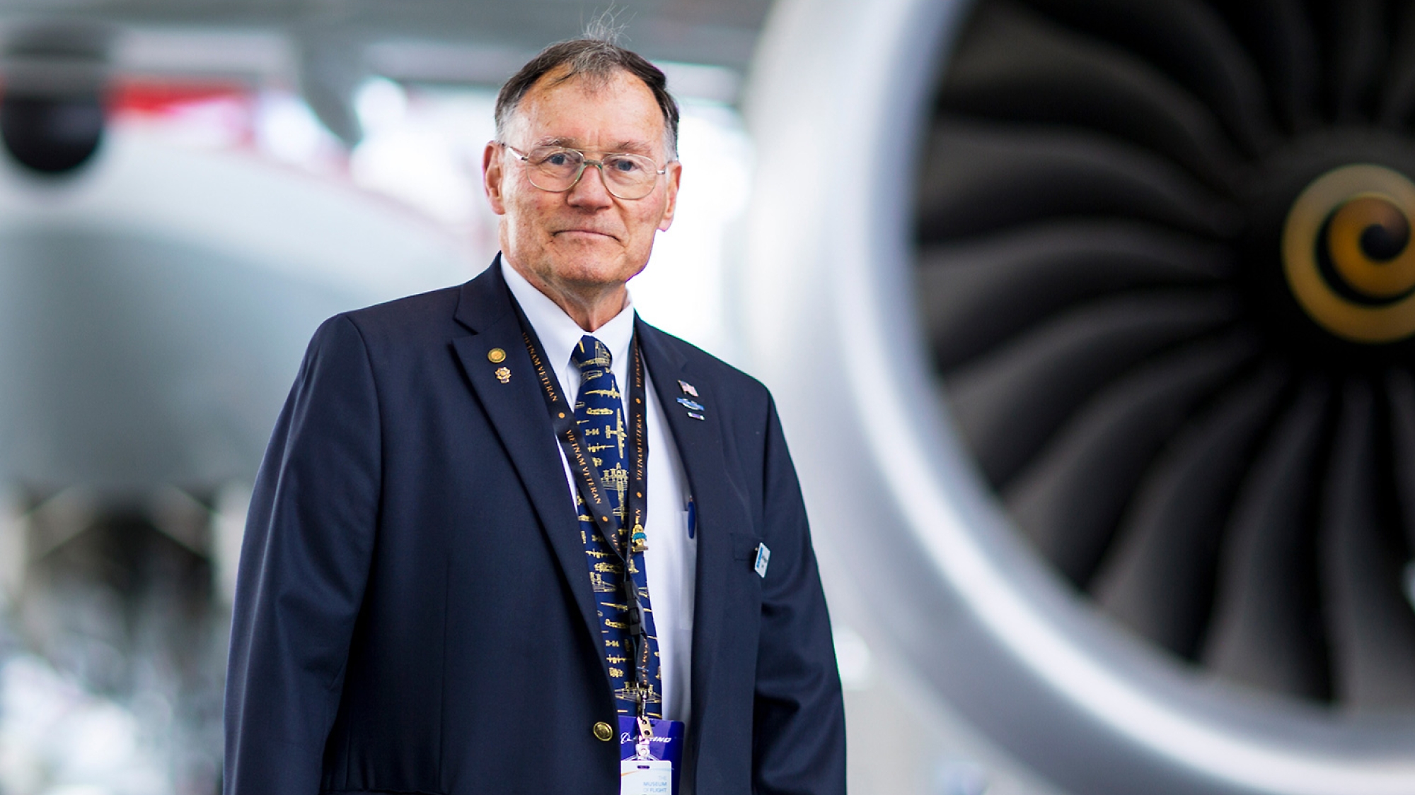 A man in a suit standing in front of an airplane engine.