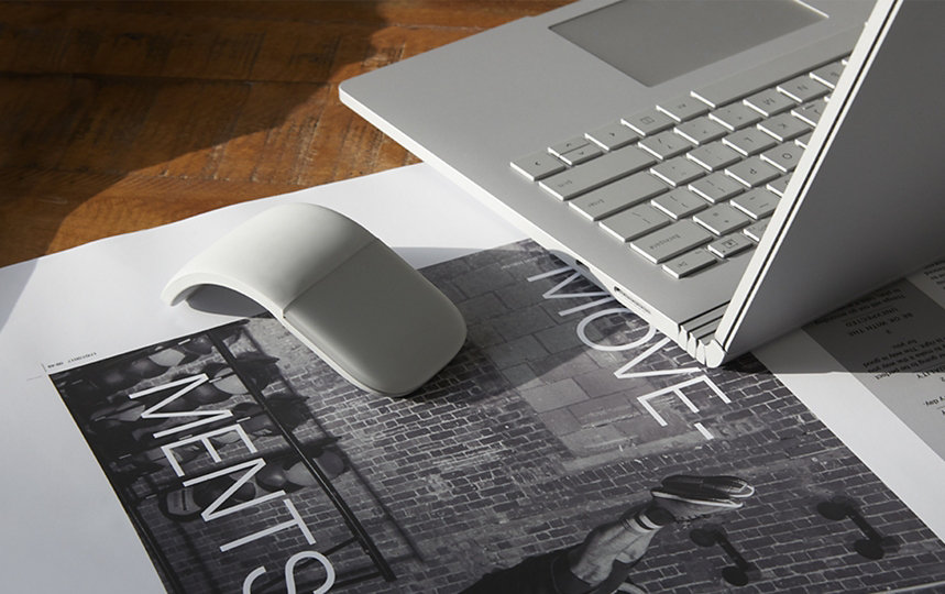 Surface Arc Mouse sits next to Surface device on a table.