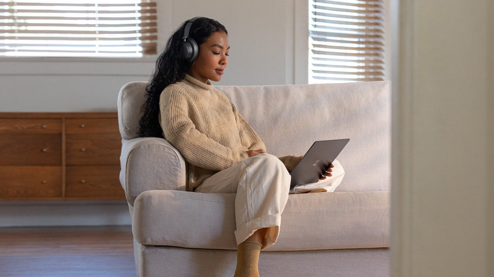 A woman wears Surface Headphones 2 while looking at a Surface computer.