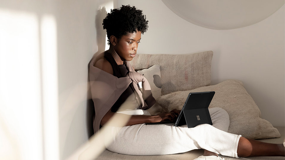 A person lounging indoors using a Signature keyboard with a Surface device.