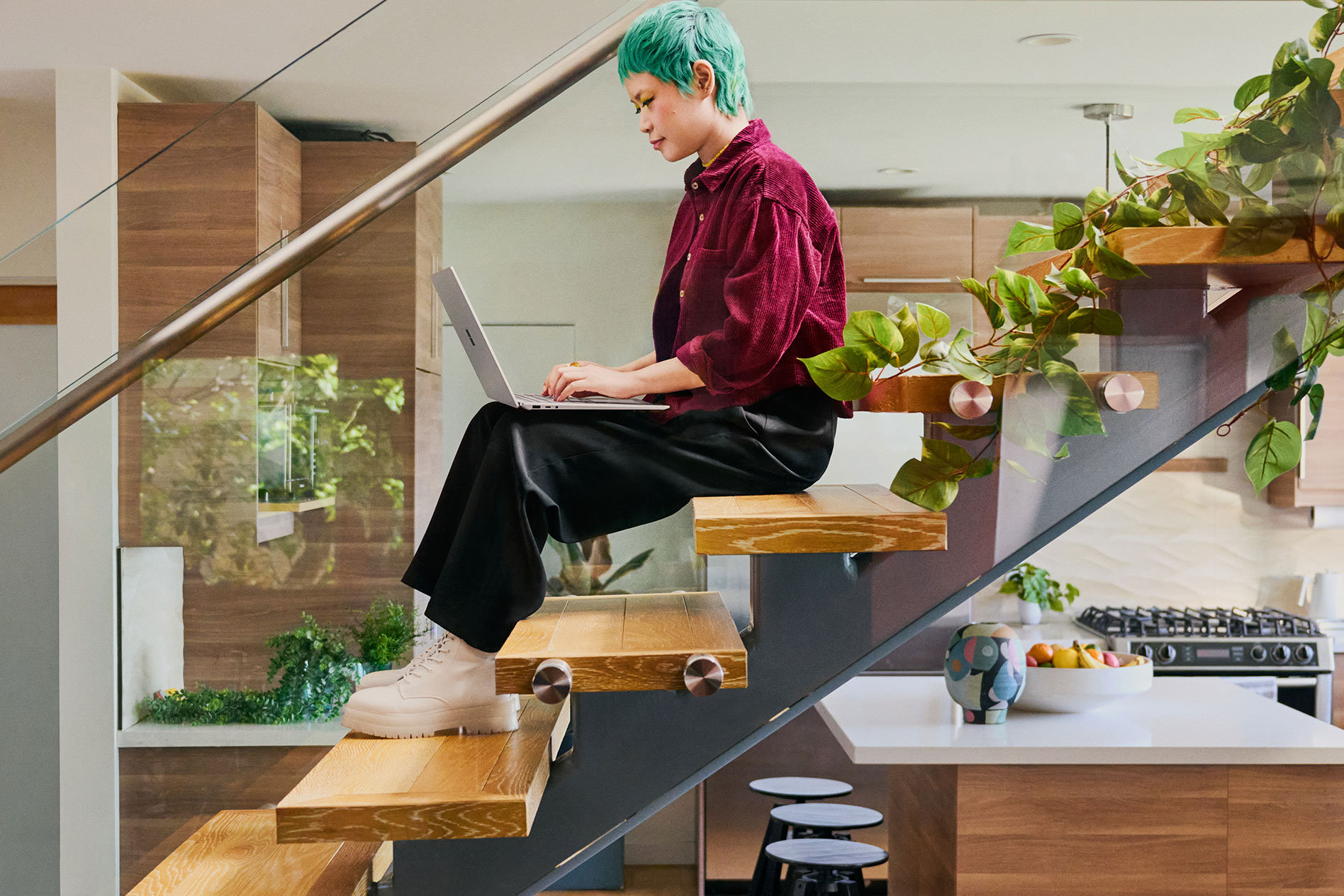 Nuori henkilö istuu portaikossa nykyaikaisessa keittiössä ja kirjoittaa Surface Laptop 5:llä.