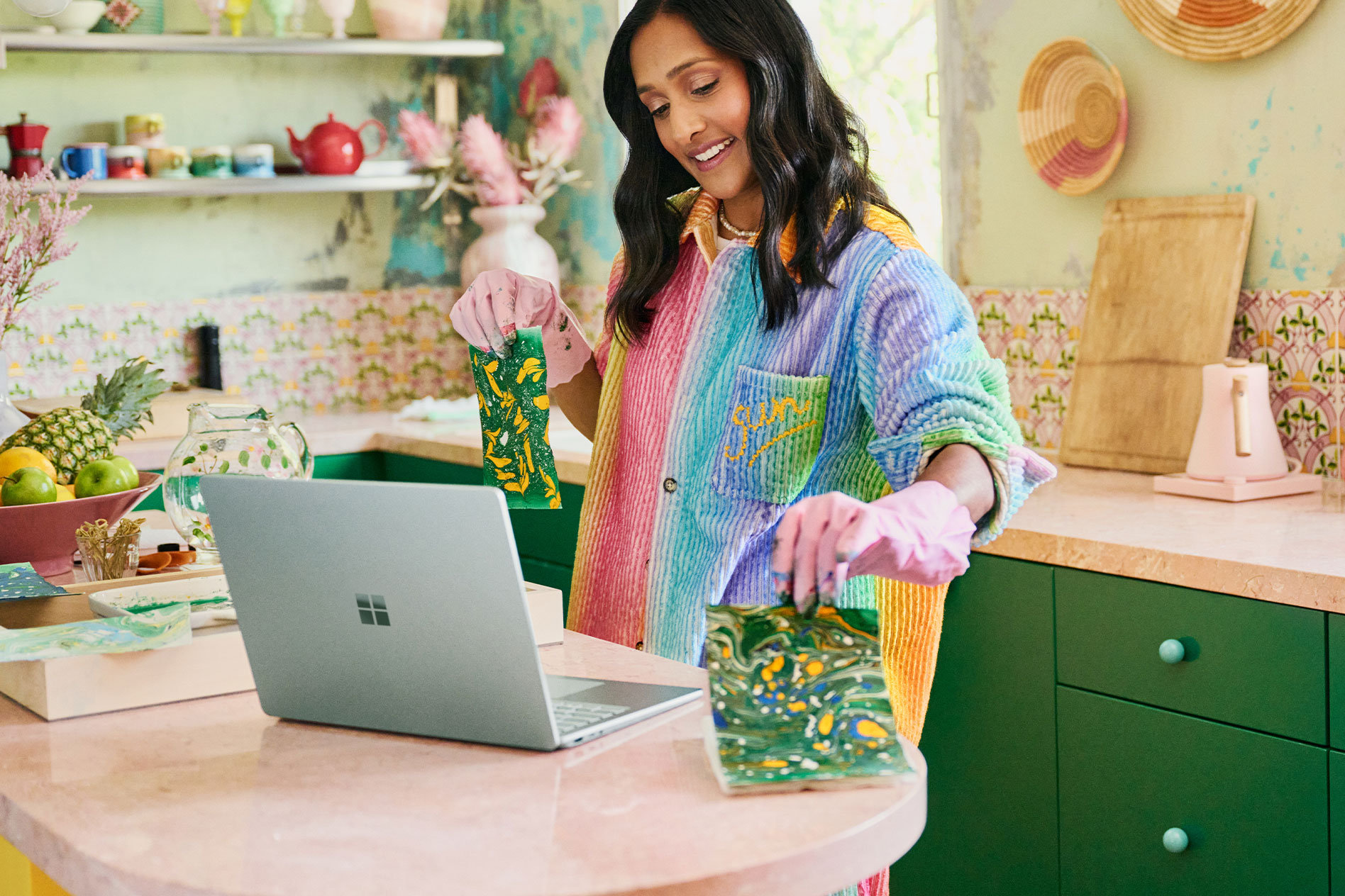 En kvinne står på et arbeidsbord og holder ting hun har laget foran kameraet på Surface Laptop 5.