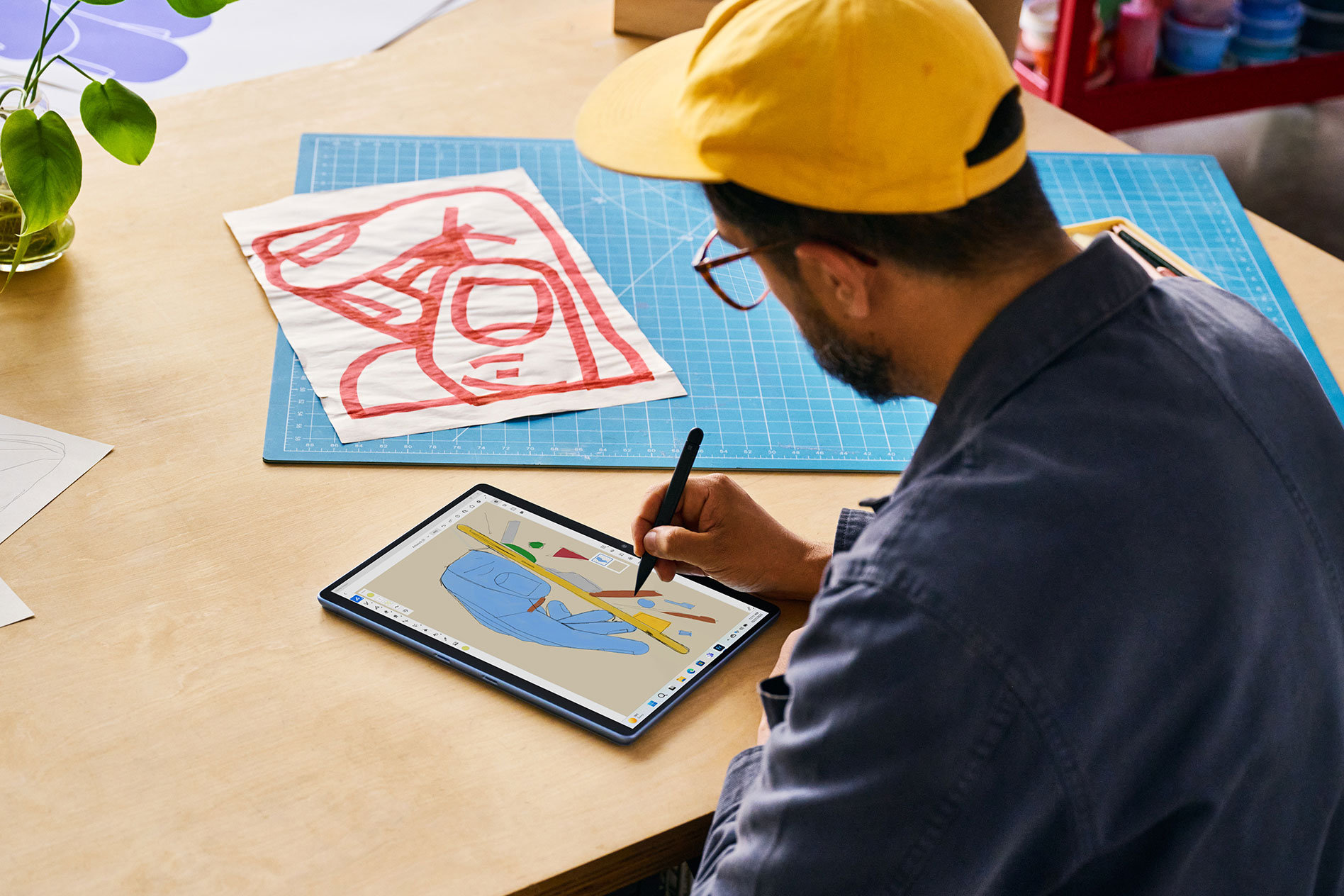 Mężczyzna w bejsbolówce siedzący przy drewnianym stole i rysujący piórem Surface Slim Pen 2 na Surface Pro 9 w trybie tabletu