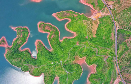 Aerial view of land with greenery and roads jetting out into a large body of water.