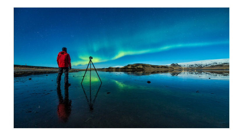 A photographer with a tripod camera prepares to capture the Northern Lights.