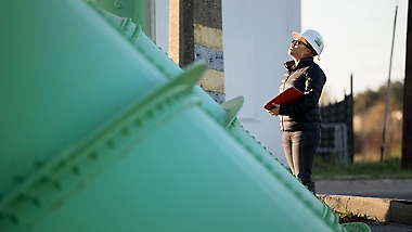 A person wearing a protective helmet looking up at large pipes.