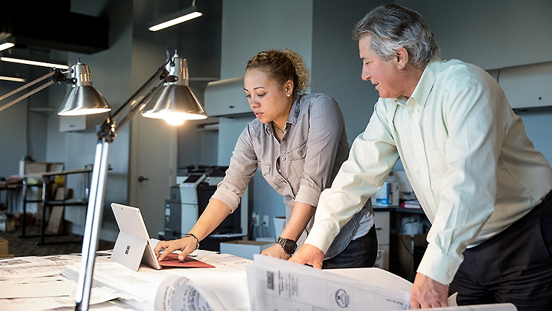 Two people looking over a desk with a tablet on it.