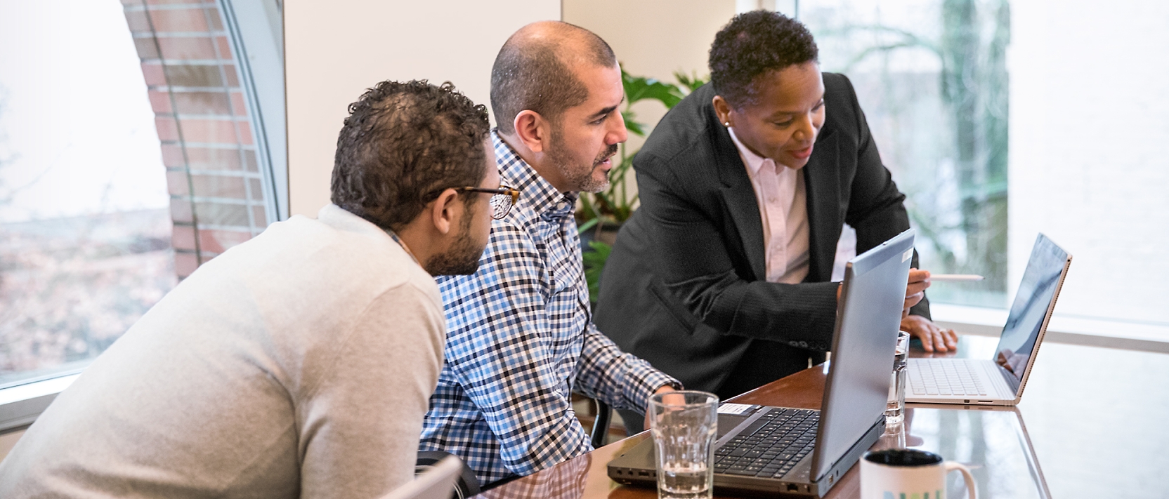 Drie mannen die rond een tafel zitten en naar laptops kijken.