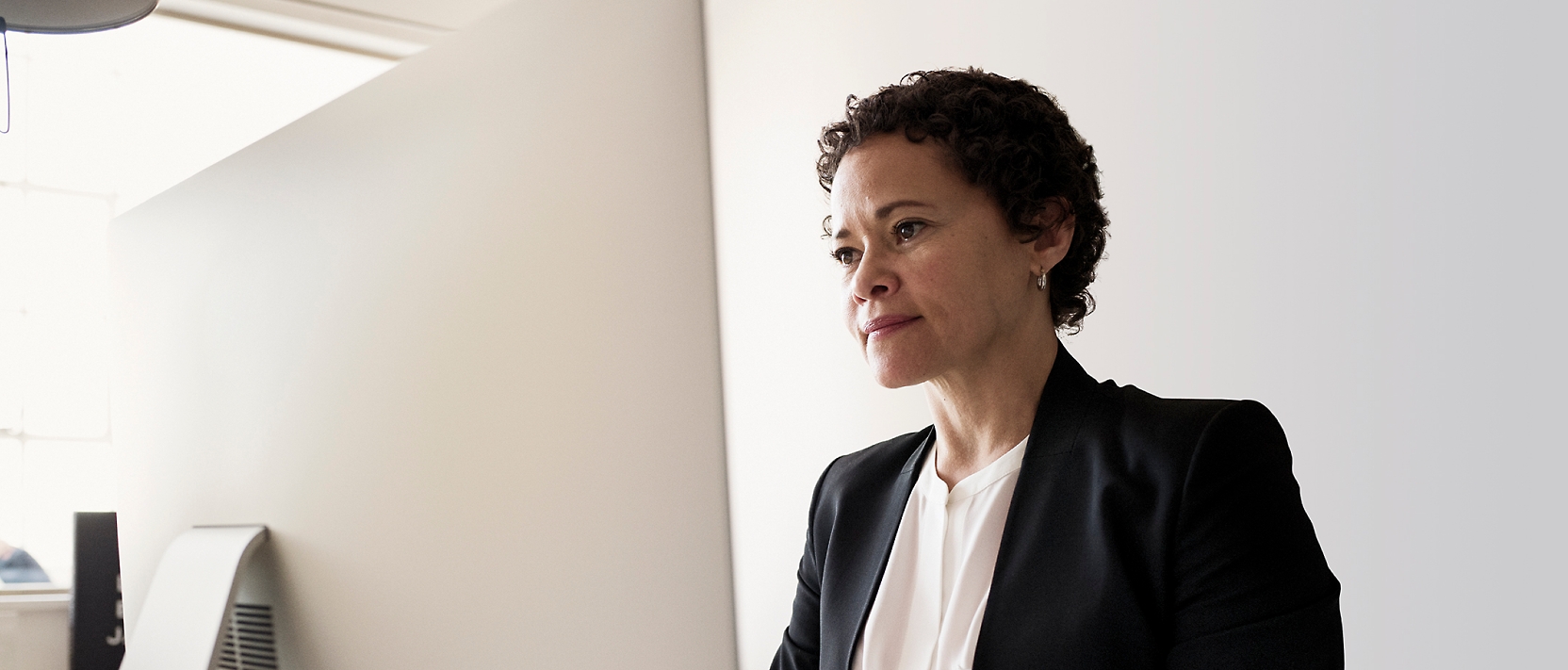 A woman in a business suit sitting in front of a computer.