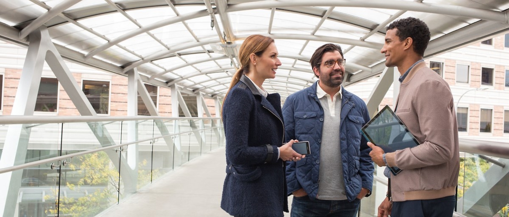 Three business people talking to each other on a walkway.