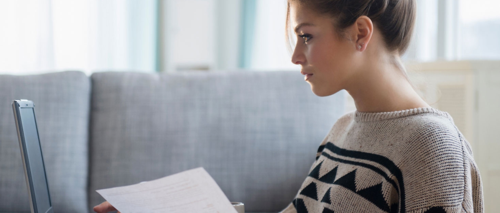 A woman is sitting on a couch looking at a laptop.