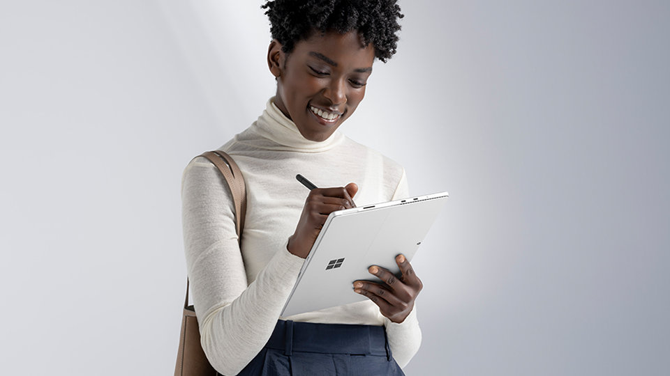 A person standing and writing with a Slim Pen on a Surface device in tablet mode.