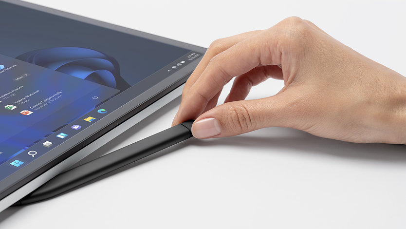 A hand pulling a Slim Pen from its dock on the side of a Surface Laptop Studio for Business.