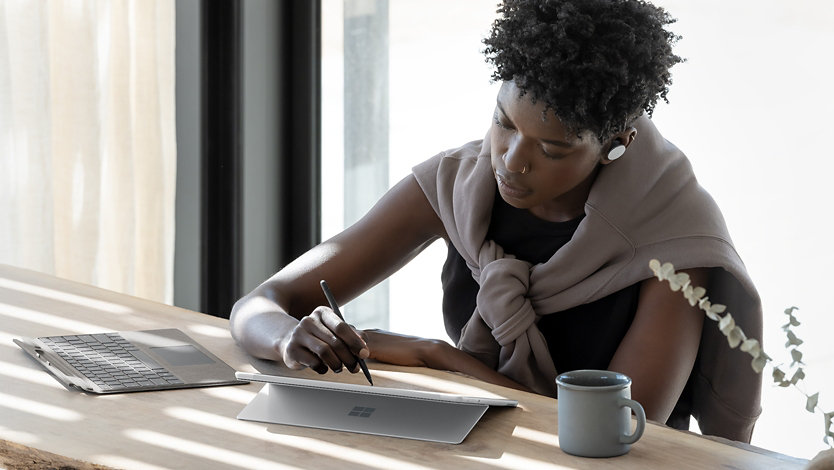 A person designing with a Surface Slim Pen at work while listening to music with Surface Earbuds.