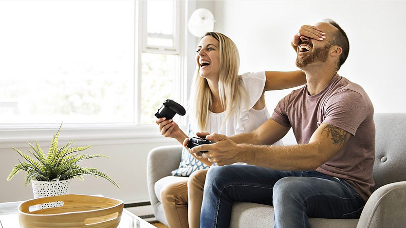 Two people use Xbox controllers on a couch.