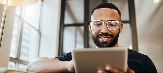 A man is wearing glasses, black tee, holding a tablet and smiling.