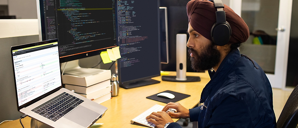 En mand med hovedtelefoner og en turban, der sidder ved et skrivebord med en computer.