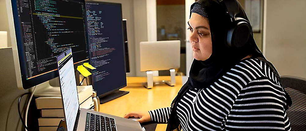 Une femme vêtue d'une chemise rayée noire et blanche et d'un hijab travaillant sur un ordinateur.